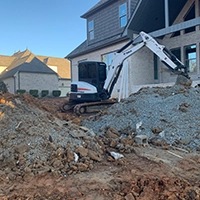 Front end loader adding stone around at a house